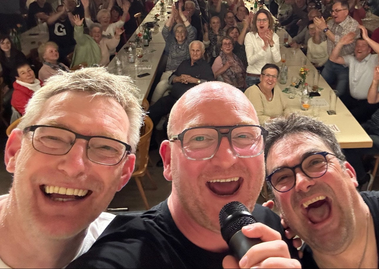 Die drei Freunde beim Auftritt, dahinter der volle Saal