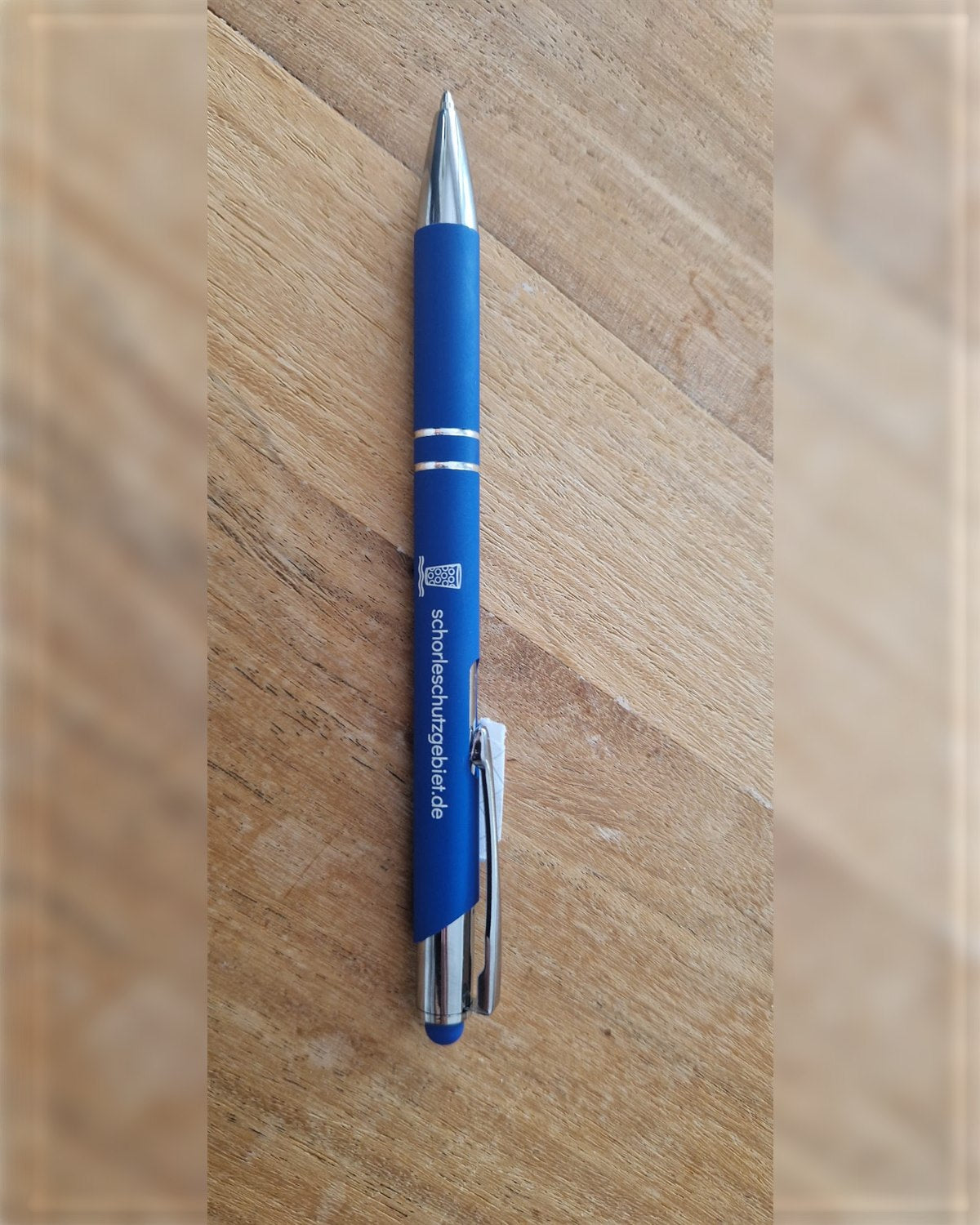 Blauer Kugelschreiber mit graviertem Dubbeglas und schorleschutzgebiet.de auf einer Holzplatte